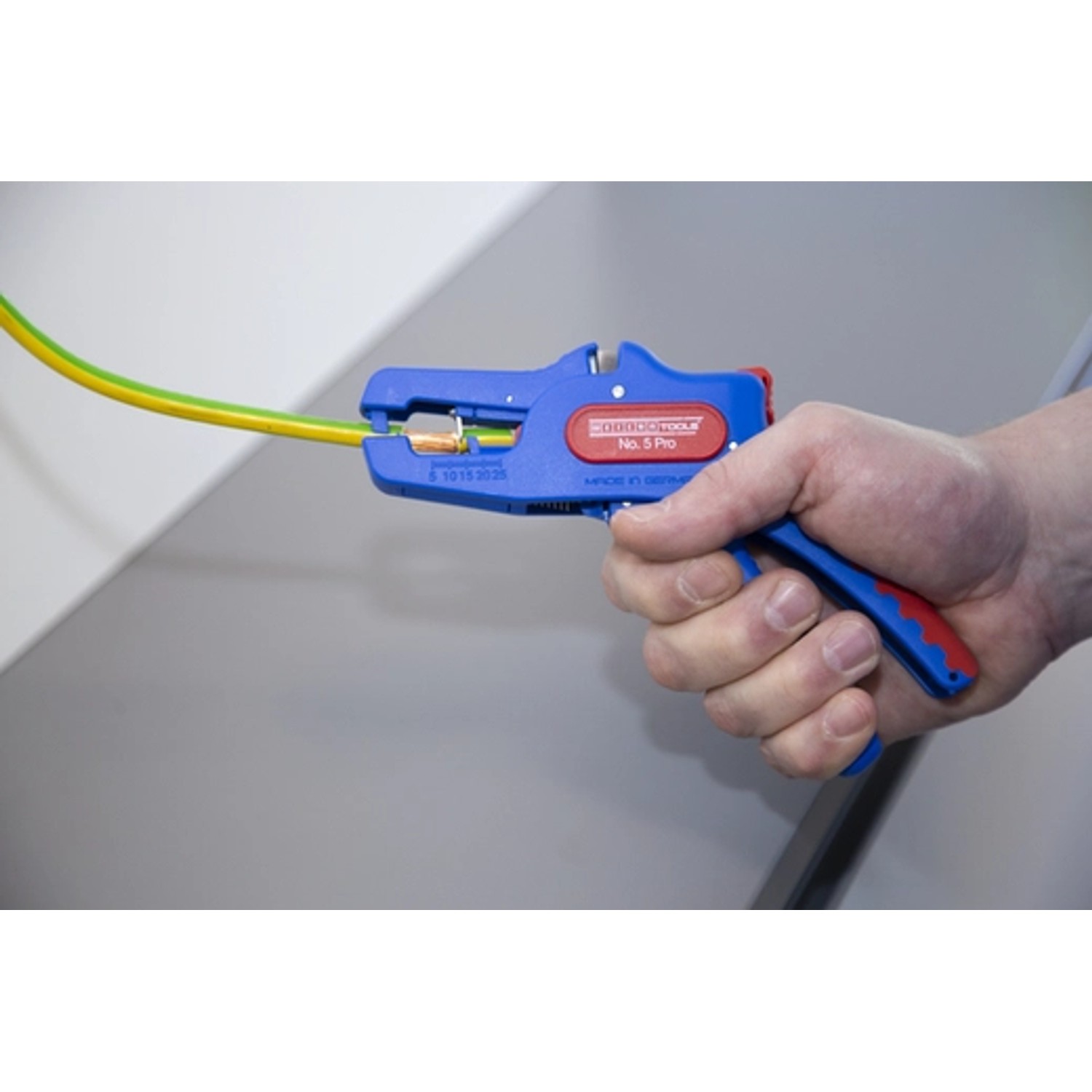 WEICON Abisolierzange No. 5 Pro in Aktion: Kabel wird abisoliert. Zange mit blau-rotem Griff.