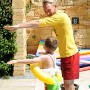 Kind mit orangem Freds Swim Academy Schwimmreifen Classic beim Schwimmtraining mit Lehrer.