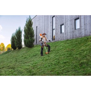 Mann mäht mit Stihl Akku-Motorsense FSA 200 Orange-Grau und Rückentrageakku einen Grashang. Für Gartenpflege.
