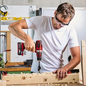 Mann bohrt mit Einhell Akku-Bohrschrauber aus dem Power X-Change Werkzeug-Set ein Loch in ein Holzbrett.