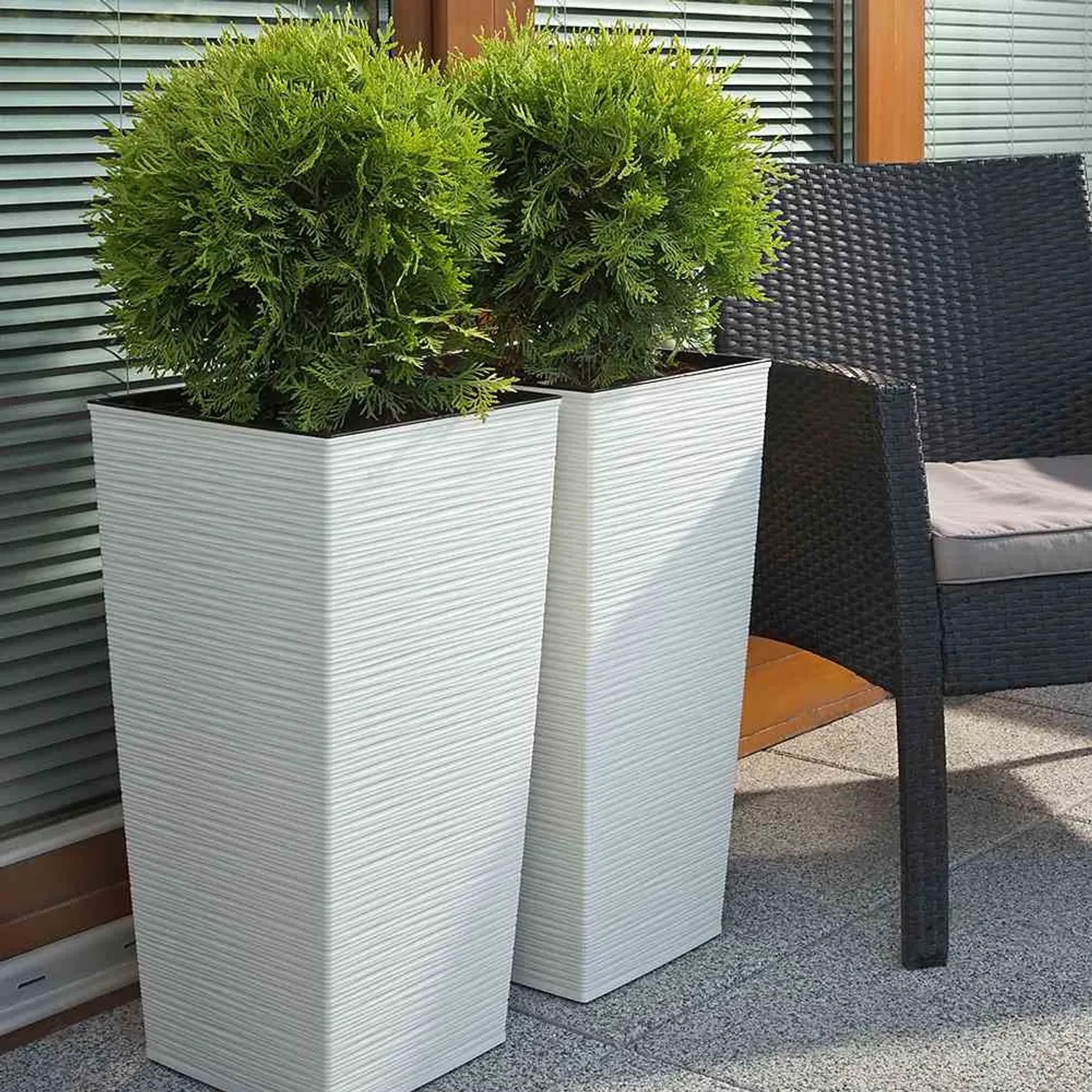 Zwei weiße Siena Garden Pflanzsäulen Nizza (35x35x68 cm) mit Rillenoptik und grünen Pflanzen.