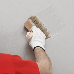 Auftragen der Stegu Grundierung mit einem Quast auf eine Wand. Haftgrund für Innen- und Außenbereiche.