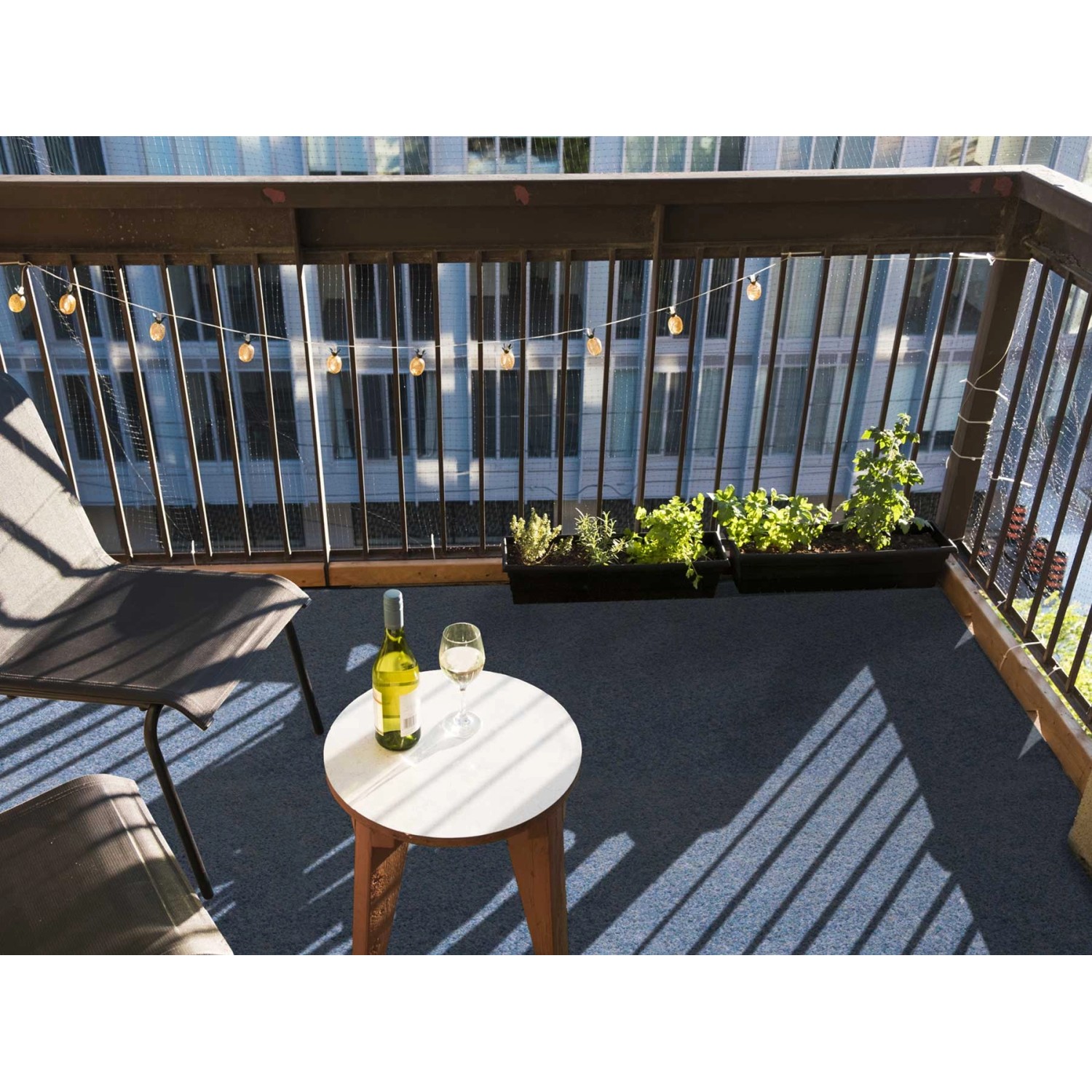 Blauer Primaflor Rasenteppich auf einem Balkon mit Tisch und Stuhl.