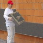 Mann verarbeitet WDVS Premium-Paket WLG 032 160 mm an einer Hauswand. Vollwärmeschutz-System.