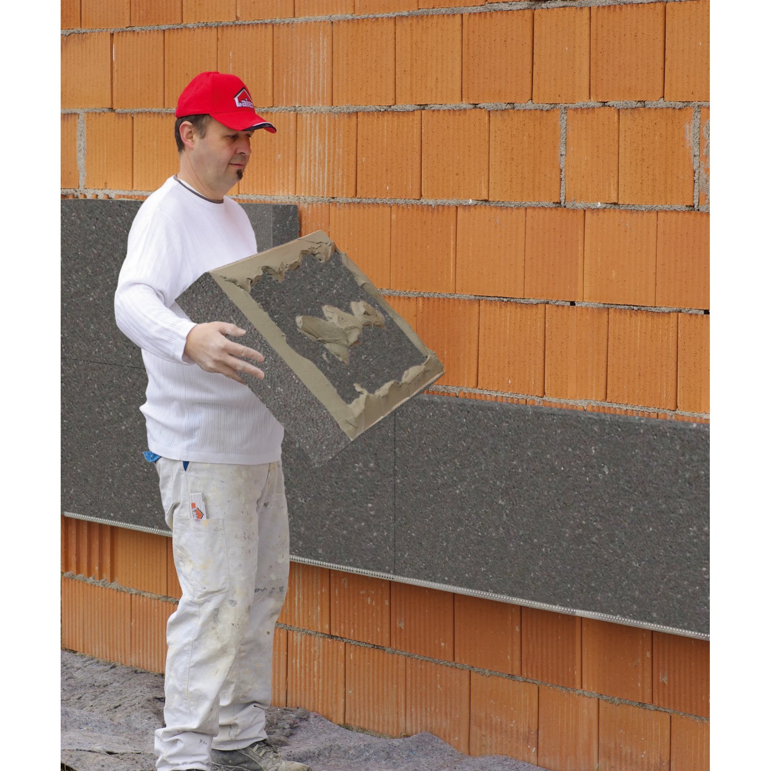 Mann verarbeitet WDVS Premium-Paket WLG 032 160 mm an einer Hauswand. Vollwärmeschutz-System.
