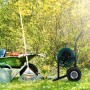 Schwarzer Relaxdays Schlauchwagen aus Metall mit grüner Schlauchtrommel und Rädern im Garten. Für Wasserschläuche.