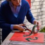 Frau schneidet Tesa Montageband für Mauerwerk mit Schere auf roter Unterlage.