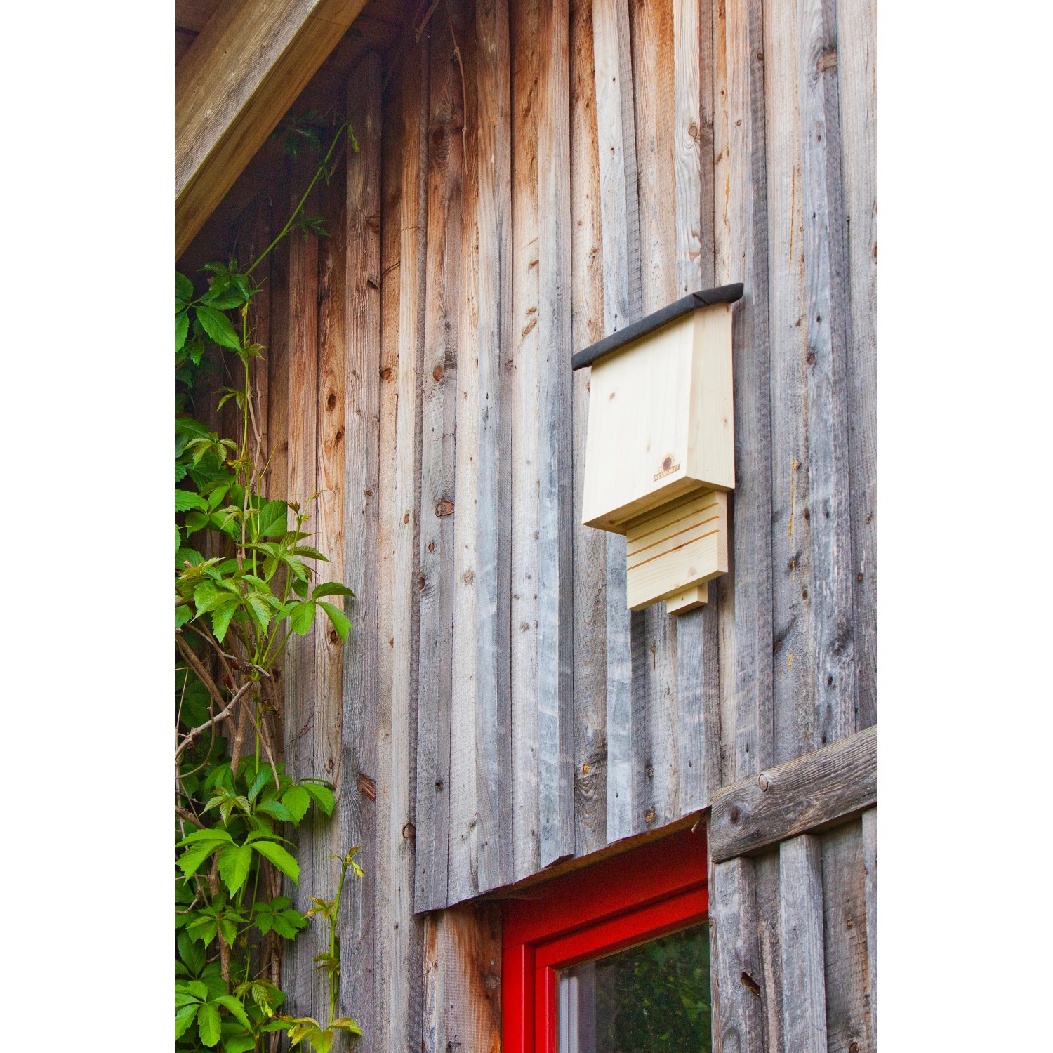 Neudorff Fledermausquartier aus Holz an einer Holzwand mit rotem Fensterrahmen.