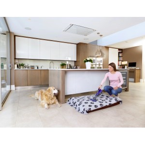 Frau saugt Tierbett mit Black+Decker Akku-Handstaubsauger Pet DVA325JP7, Hund liegt daneben.