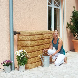 Garantia Wandtank Rocky 400 l Sandstone mit Frau und Gießkanne vor Hauswand. Regentonne in Steinoptik.