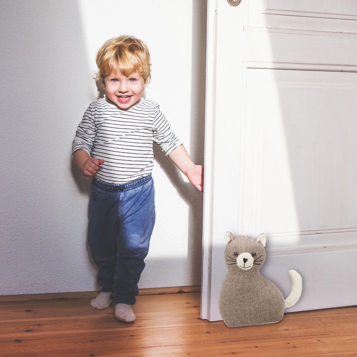 Brauner Türstopper Katze aus Polyester hält weiße Tür offen. Kind lächelt im Hintergrund. Dekorativer Türpuffer für Kinderzimmer.