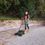 Frau kehrt mit Kärcher Kehrmaschine S 4 Twin Go!Further Laub auf gepflasterter Fläche.