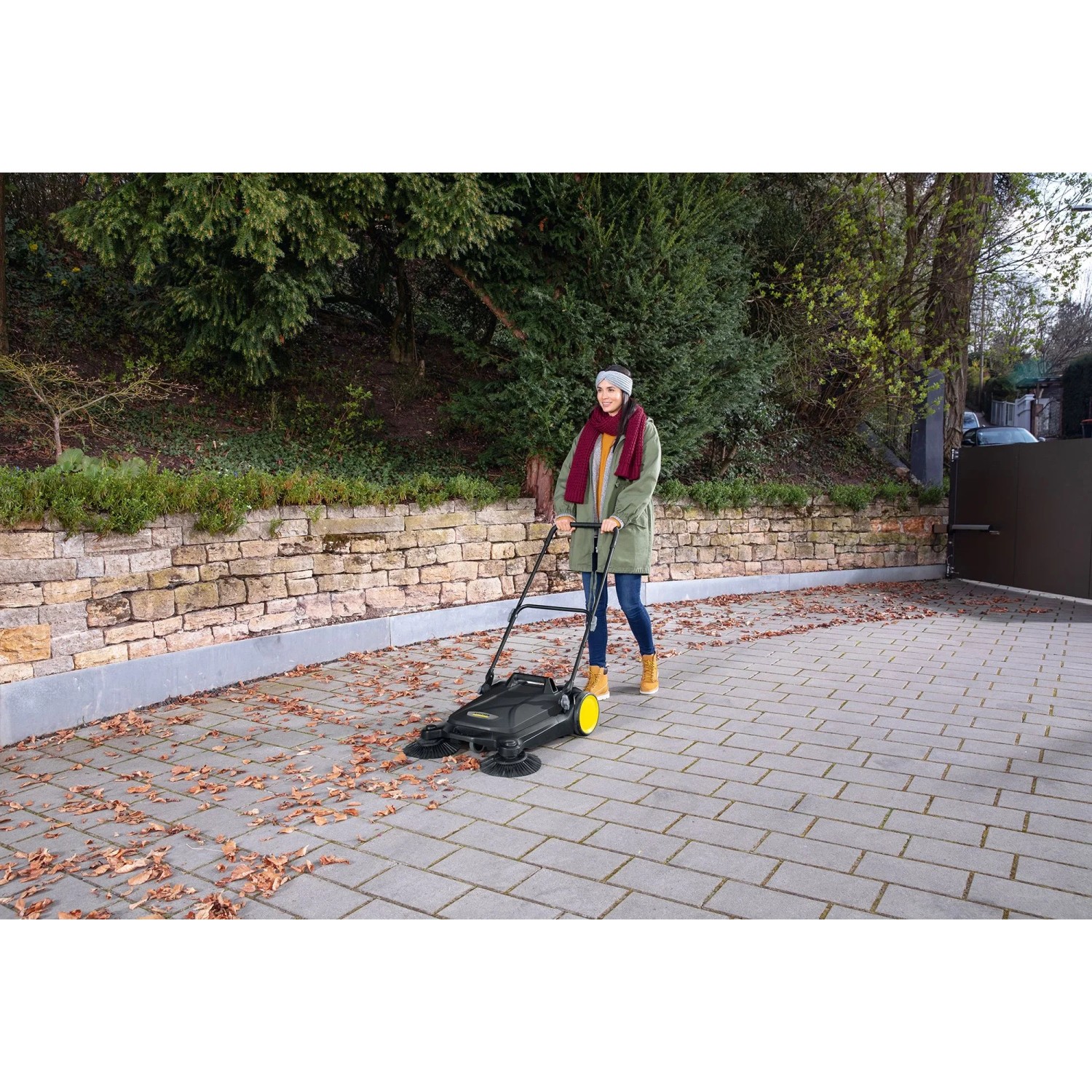 Frau kehrt mit Kärcher Kehrmaschine S 4 Twin Go!Further Laub auf gepflasterter Fläche.