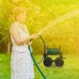 Schwarzer Relaxdays Gartenschlauchwagen aus Stahl mit Kurbel und 4 Rädern, im Garten beim Bewässern.