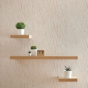 Cremefarbene Vliestapete mit feinem Wellenmuster an einer Wand, dekoriert mit Holzregalen und Pflanzen.