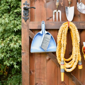 Gelber Hozelock SuperHoze Expansions-Gartenschlauch (15m) hängt an einer Holzwand mit Gartengeräten.