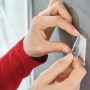 Anbringen eines Tesa Powerstrips Haken Waterproof eckig Edelstahl Large an einer grauen Wand.