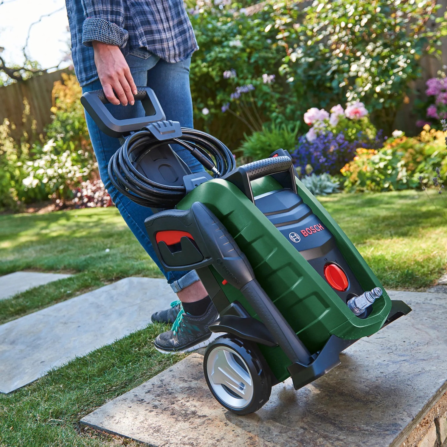 Bosch UniversalAquatak 125 Hochdruckreiniger in Grün mit Schlauch und Griff auf Steinplatten.