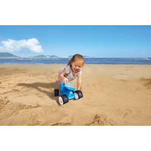 Kind spielt mit blauem Hape Dünen-Buggy Sandspielzeug am Strand.