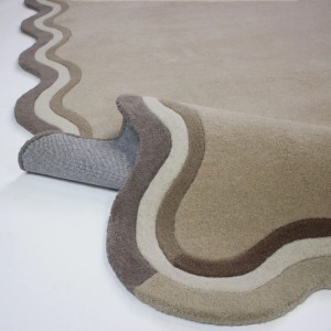 Flair Rugs Wollteppich Leo Border aus Wolle in Naturtönen, mit handgefertigten Wellenkanten. Teilweise aufgerollt.