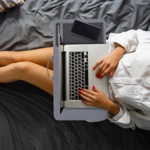Graues Relaxdays Laptopkissen mit Mauspad, Handyhalterung und Tragegriff. Person arbeitet bequem im Bett.