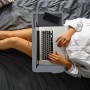 Graues Relaxdays Laptopkissen mit Mauspad, Handyhalterung und Tragegriff. Person arbeitet bequem im Bett.