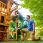 Zwerkules Spielturm Bolzo mit Rutsche und Schaukel: Kind klettert Leiter hoch, Vater schaut zu.