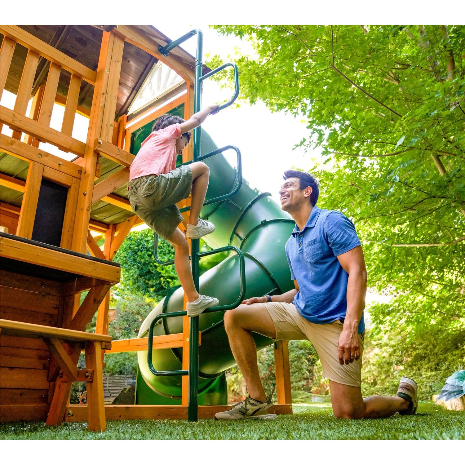 Zwerkules Spielturm Bolzo mit Rutsche und Schaukel: Kind klettert Leiter hoch, Vater schaut zu.