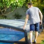 Graue Palram Canopia Poolüberdachung Majorca (458x677cm) wird von einer Person geöffnet.