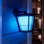 Hängende Philips Hue Econic LED-Laterne in Schwarz mit blauem Licht an Hauswand.