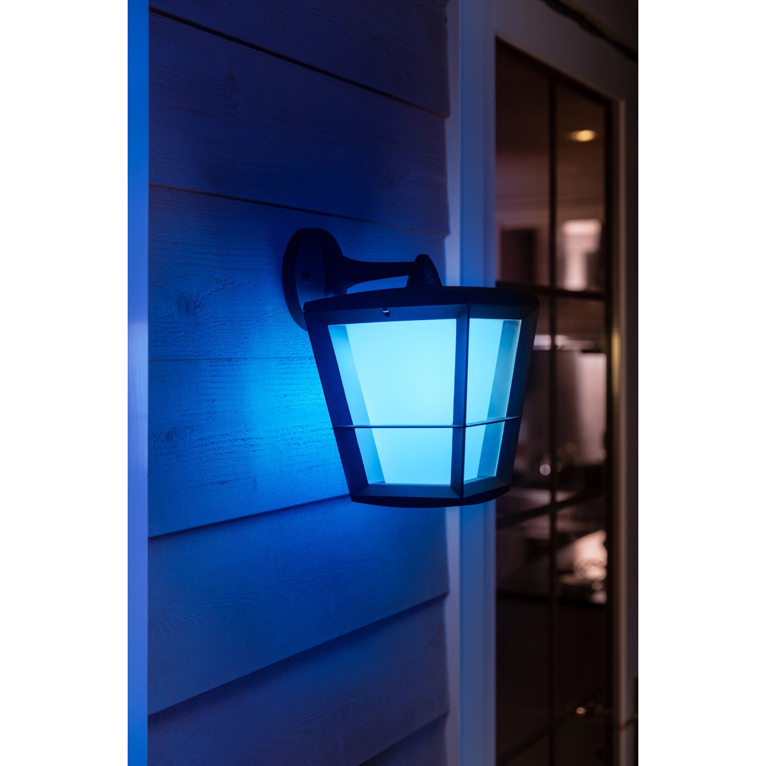 Hängende Philips Hue Econic LED-Laterne in Schwarz mit blauem Licht an Hauswand.