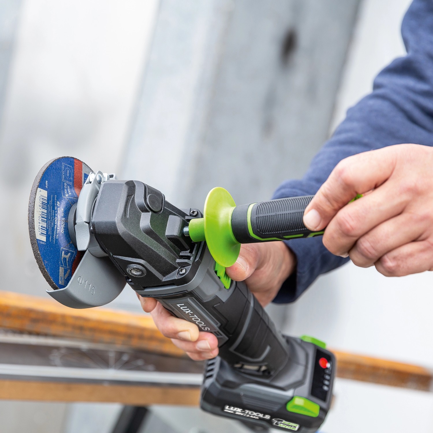 LUX Akku-Winkelschleifer im Einsatz, Teil des 3in1 Akku-Maschinensets. Schleifscheibe und Zusatzhandgriff sichtbar.