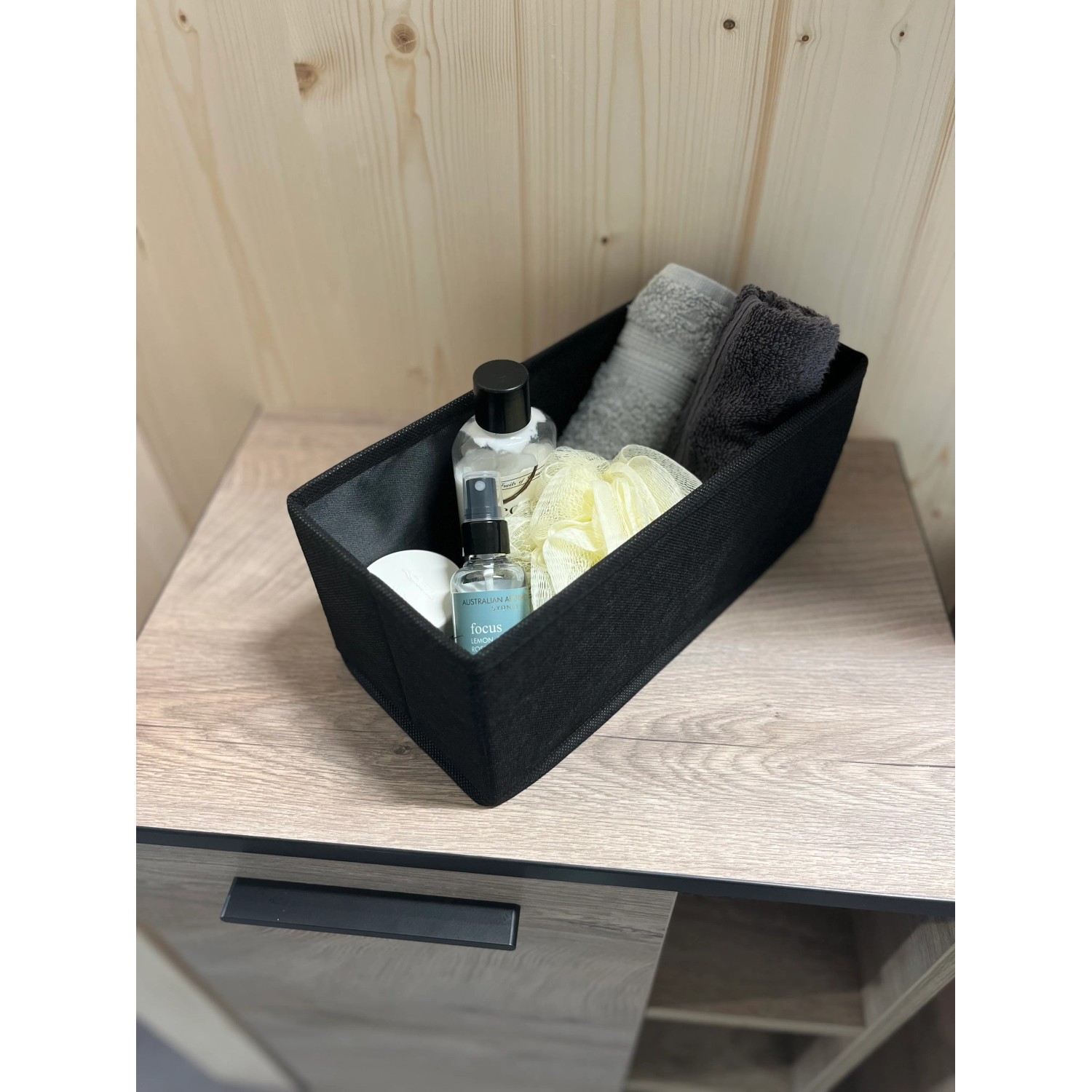 Schwarzes Fackelmann Universalkörbchen Textil (13x12x28cm) mit Badutensilien auf einem Waschtisch.