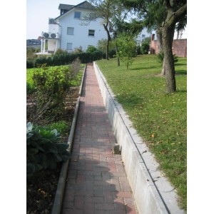 Graue Mähkante aus Beton (24x12x4,5 cm) als Rasenkante in einem Garten.