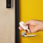 Hand hält Fernbedienung für Yale Alarmanlage Smart Alarm Starterkit vor gelber Tür.