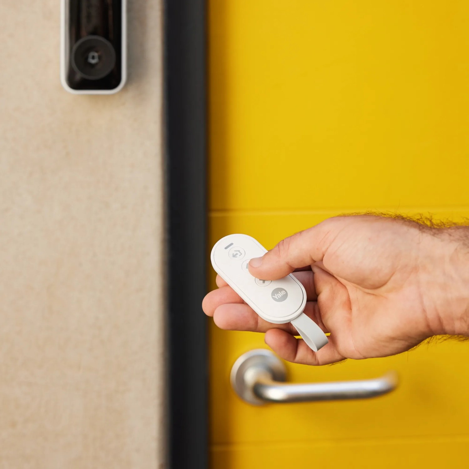 Hand hält Fernbedienung für Yale Alarmanlage Smart Alarm Starterkit vor gelber Tür.