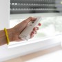 Hand mit Schellenberg Funk-Handsender (1-Kanal, weiß) zur Rollladensteuerung vor Fenster.