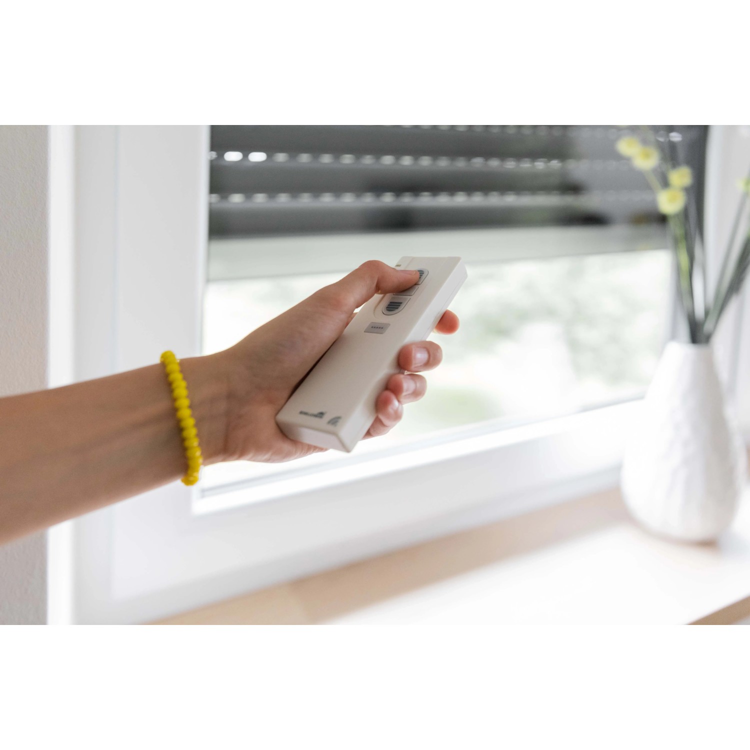 Hand mit Schellenberg Funk-Handsender (1-Kanal, weiß) zur Rollladensteuerung vor Fenster.