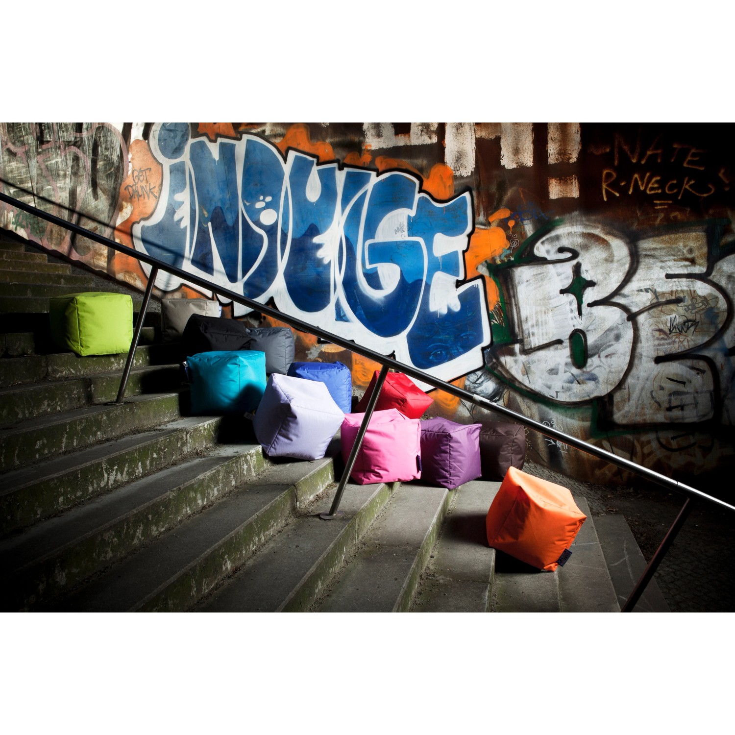 Mehrere farbige Sitting Point Hocker Scuba (60 l) auf einer Treppe vor Graffiti-Wand.