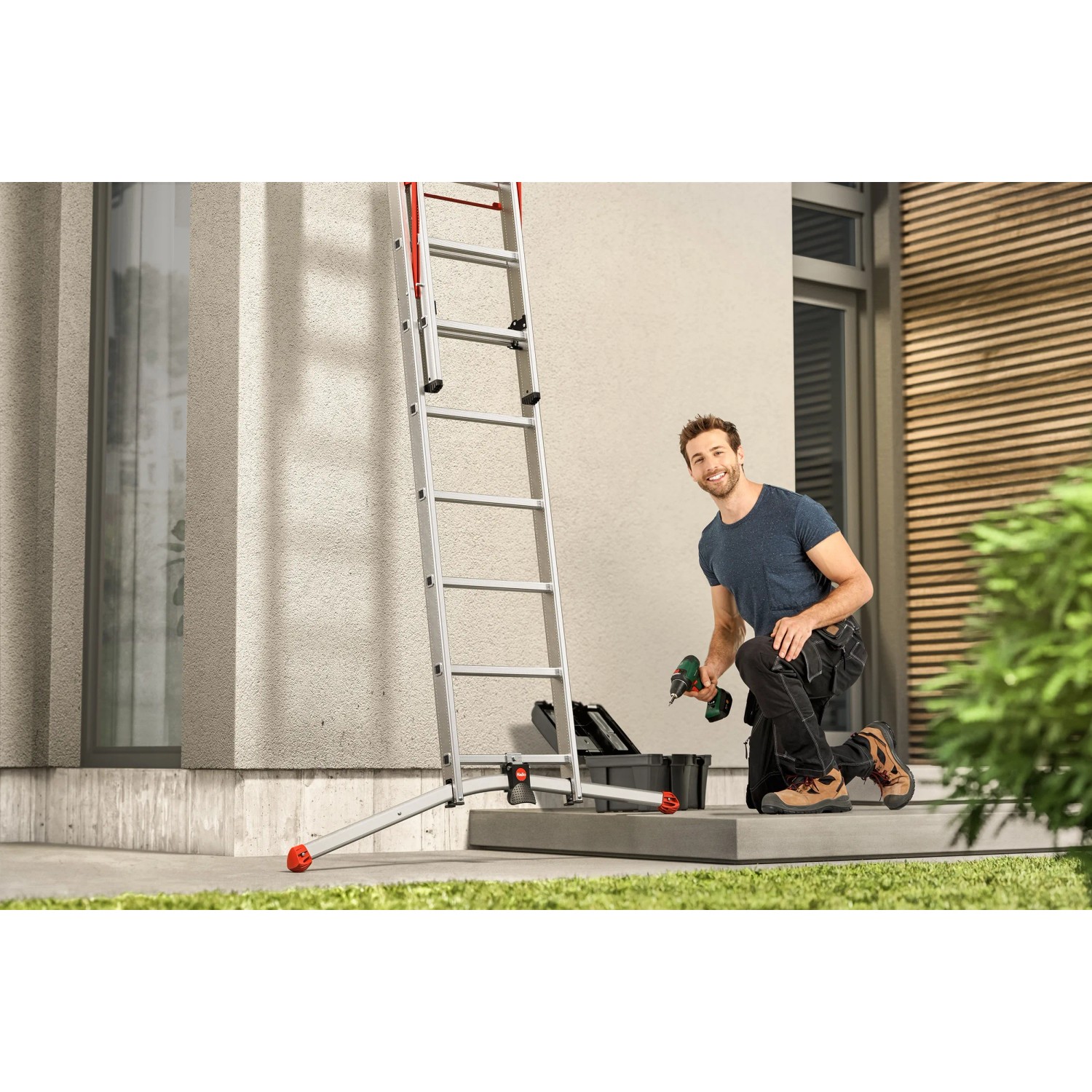 Hailo Alu-Kombileiter S100 Profi Lot im Einsatz mit Mann und Werkzeug vor Hauswand.