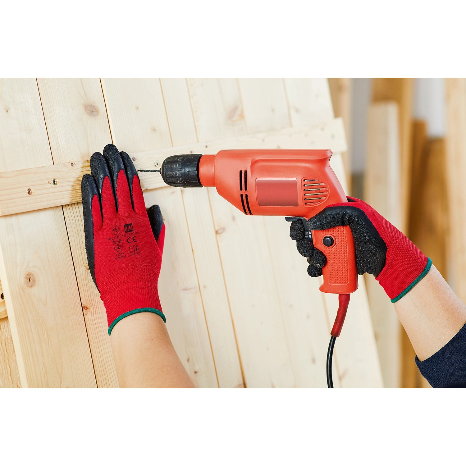Hände mit roten Arbeitshandschuhen bohren in Holz. Arbeitshandschuhe Latex Größe 8.