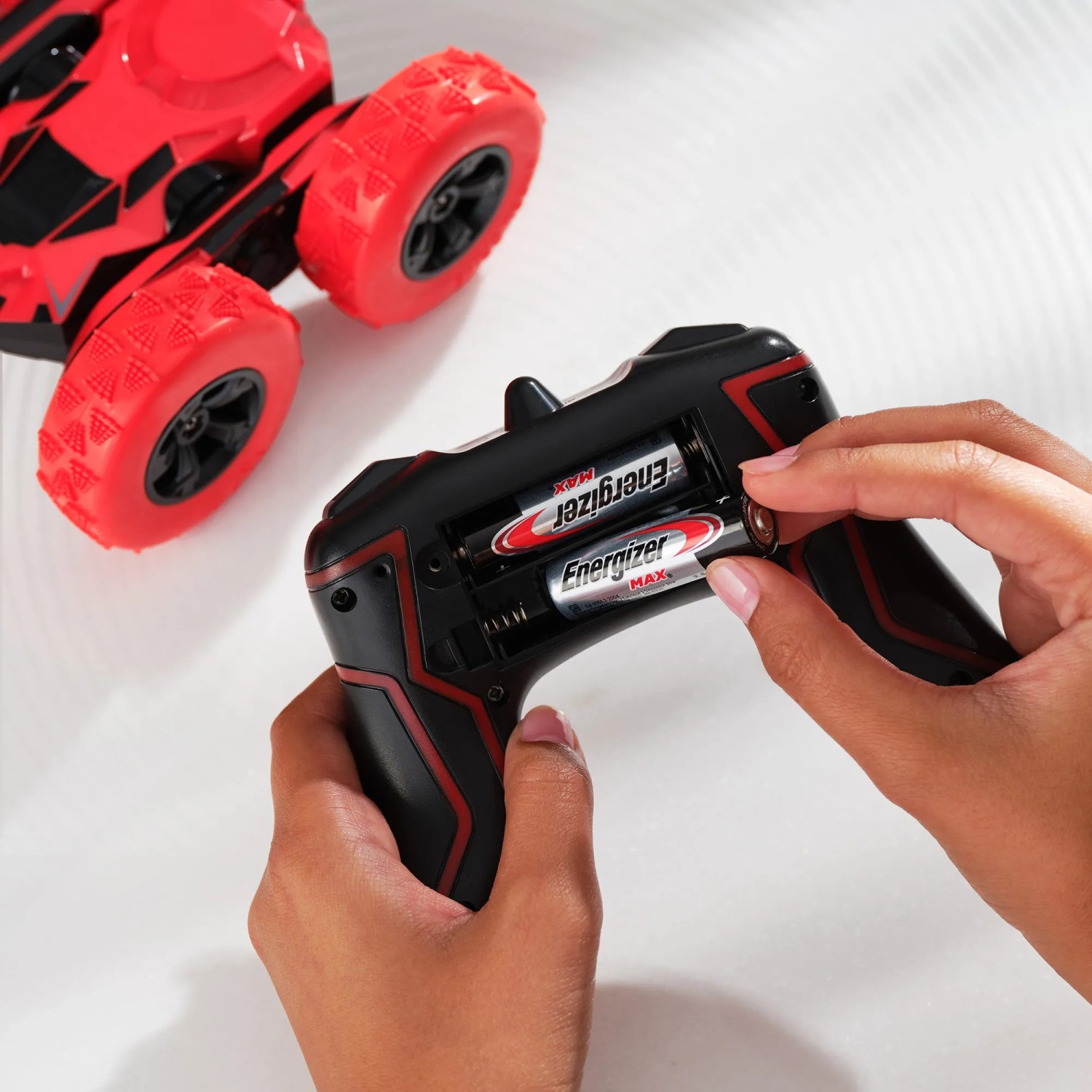 Einsetzen von Energizer AA Batterien in eine Fernbedienung, mit rotem Spielzeugauto im Hintergrund.