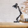 Schwarze Metall Schreibtischlampe im Industrial Design mit schwenkbarem Gelenkarm auf Holzschreibtisch vor Ziegelwand.