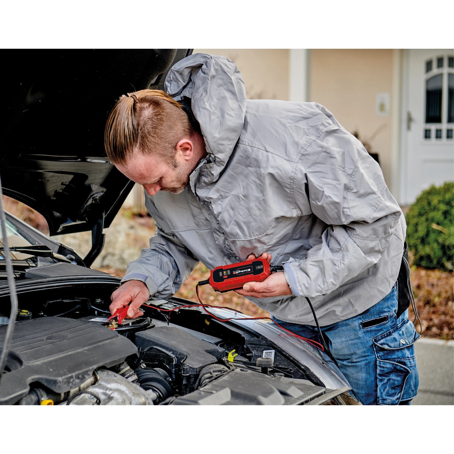 Mann schließt Einhell CE-BC 1 M Batterieladegerät an Autobatterie an.