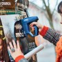 Frau tackert Poster mit blauem Rapid Akku-Tacker BTX10 an Plakatwand.