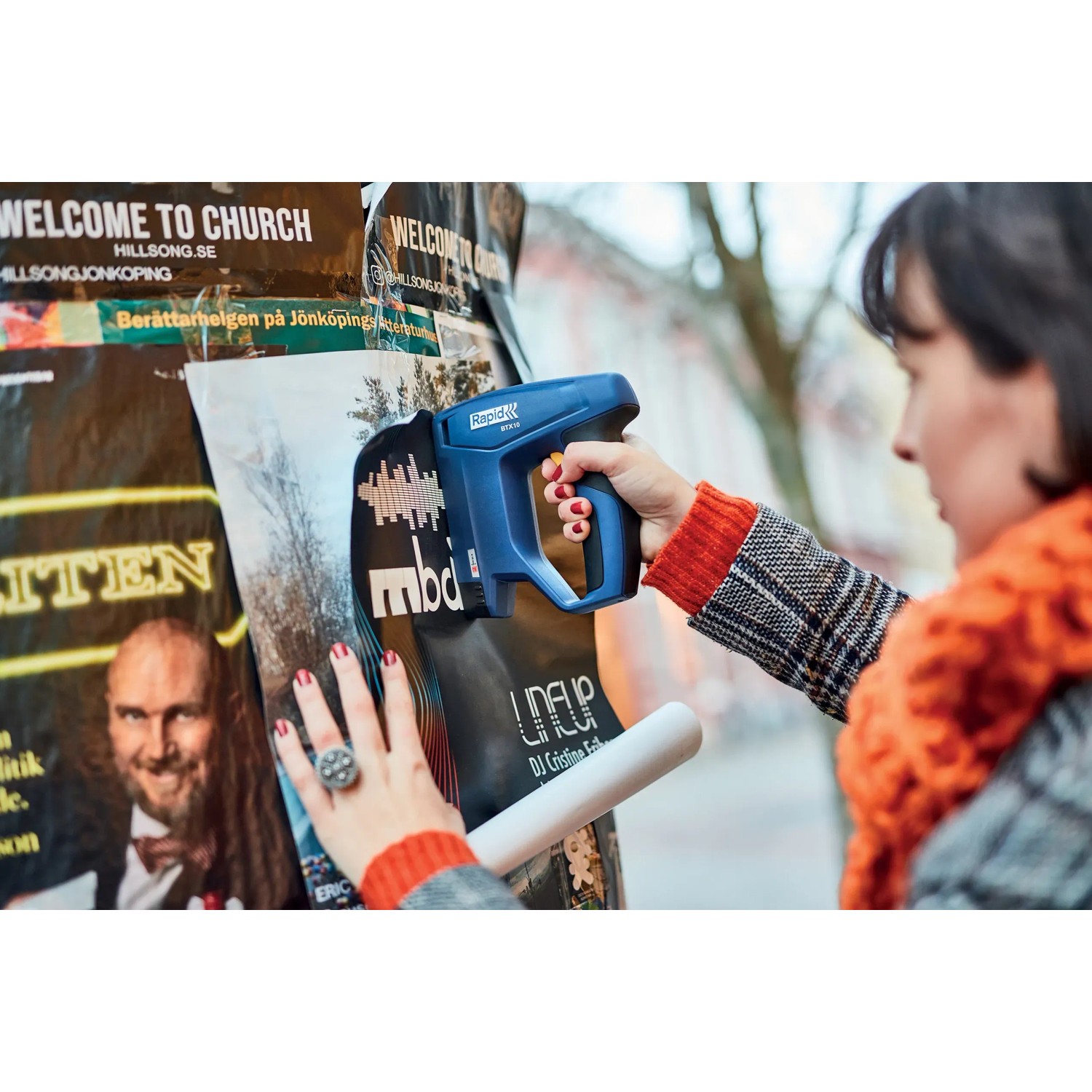 Frau tackert Poster mit blauem Rapid Akku-Tacker BTX10 an Plakatwand.