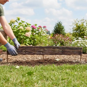 Braune Relaxdays Beeteinfassung aus Weide (10er Set) wird in einem Garten aufgebaut.