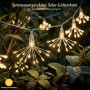 Solar LED Feuerwerk Lichterkette in warmweißem Licht, spritzwassergeschützt, hängt im Garten zwischen Blättern mit Tautropfen.