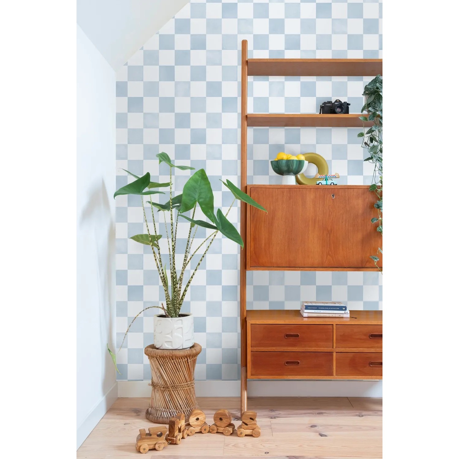 ESTAhome Tapete mit blauem Karomuster an einer Wand. Modernes Interieur mit Pflanze und Holzregal.