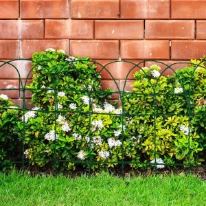 Grünes Karat Ziergeflecht als Beetbegrenzung vor einer Ziegelmauer.